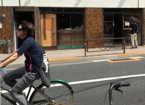 湯立て坂を下って千川通りにぶつかる手前。自転車が走り、店内をのぞくひとも。